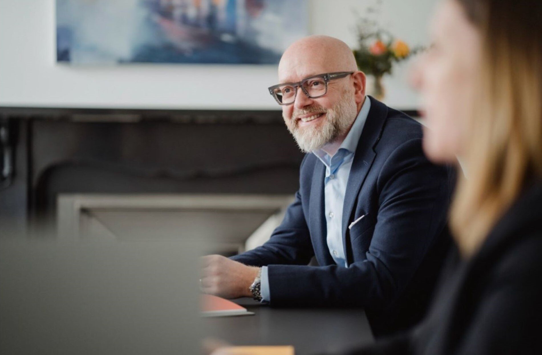 An image of an AAB employee wearing a suit and sitting at an office desk smiling. An image of an AAB employee wearing a suit and sitting at an office desk smiling.