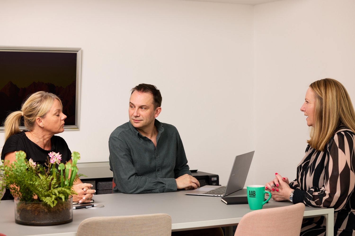 An image of three AAB employees sitting at a desk with their laptops and having a converation.