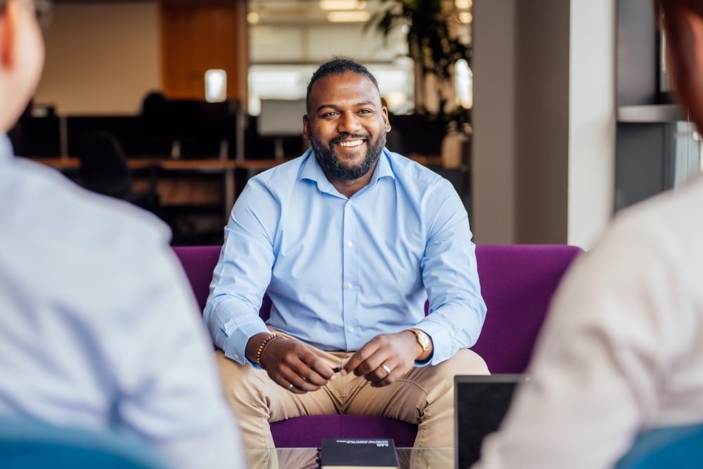 AAB employee sitting on couch wearing blue shirt smiling and listening