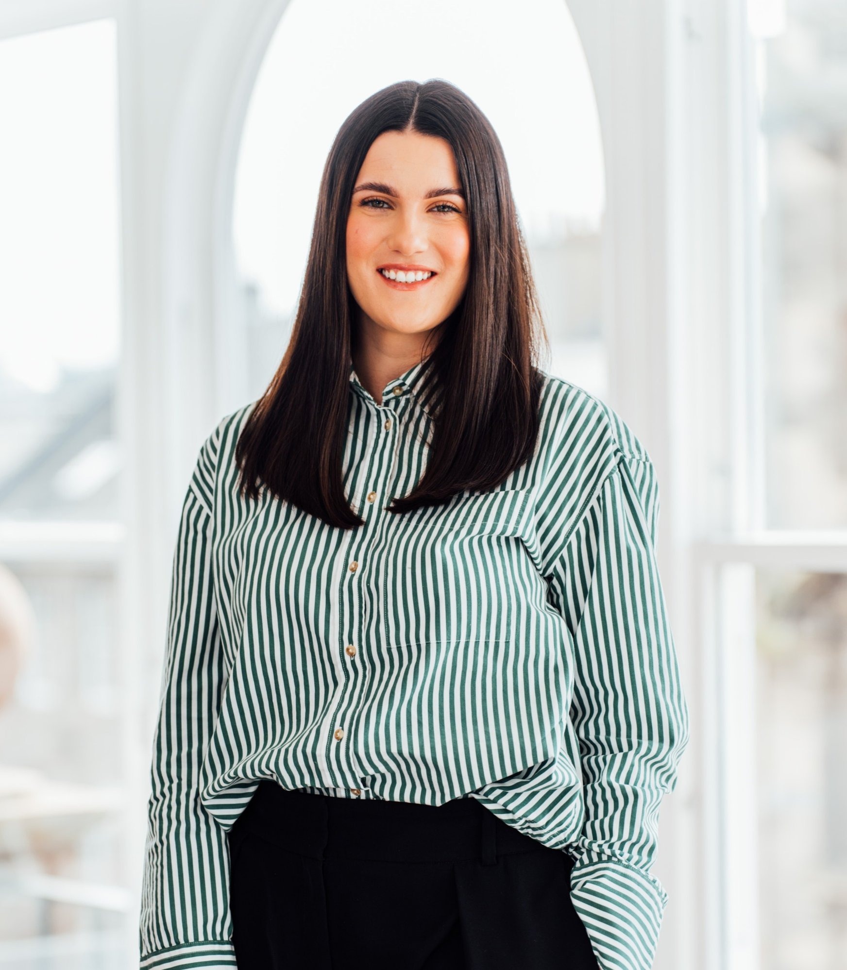 An image of Alix Baird wearing a green and white striped shirt and is smiling at the camera. An image of Alix Baird wearing a green and white striped shirt and is smiling at the camera.