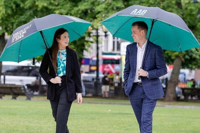 An image of two AAB employees walking outside holding AAB branded umbrellas. An image of two AAB employees walking outside holding AAB branded umbrellas.
