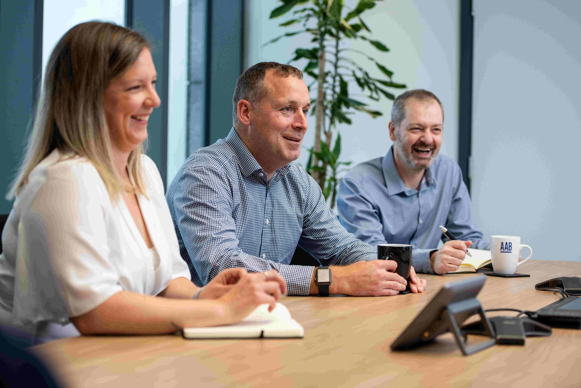 Three team members laughing and smiling round a desk in a meeting room