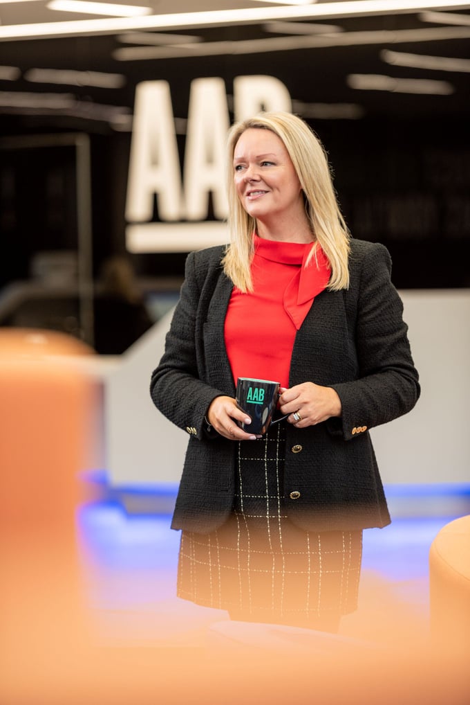 An image of an AAB employee wearing a red top and black skirt and carrying an AAB branded mug, An image of an AAB employee wearing a red top and black skirt and carrying an AAB branded mug,