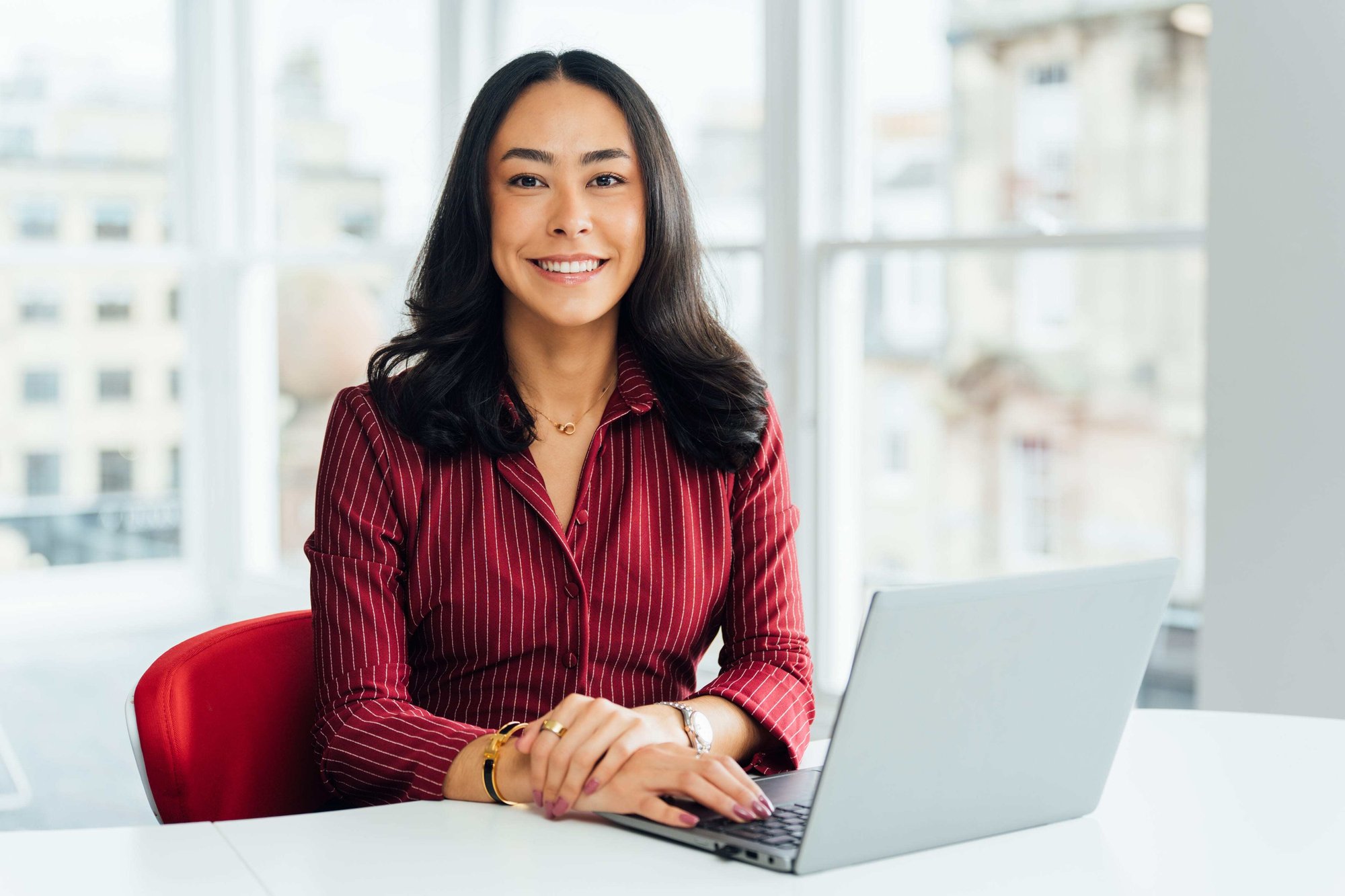 An image of Hannah Wildsmith wearing a burgandy shirt and sitting at the desk with her laptop.