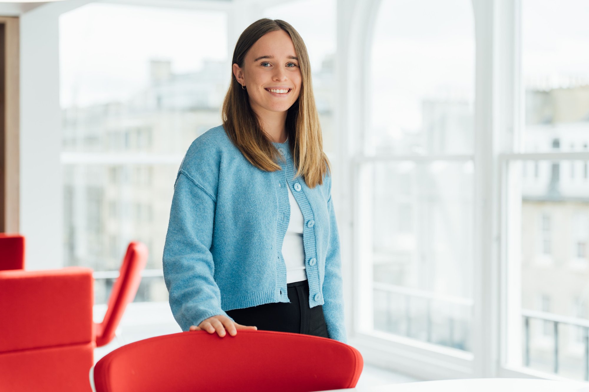 An image of Louise Neilson wearing a blue cardigan and white top. She is standing in the Edinburgh office.