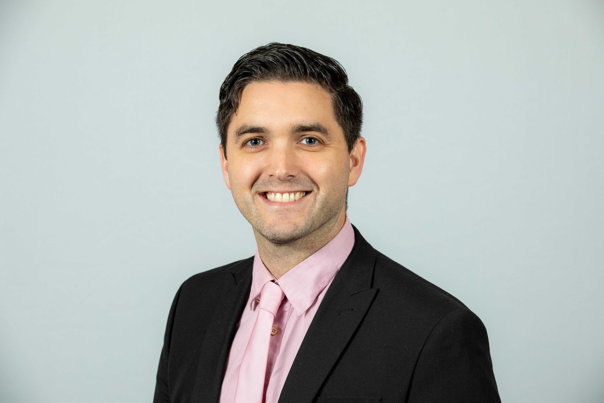 An image of Mark McCluskey wearing a pink tie and pink shirt. He is smiling at the camera.