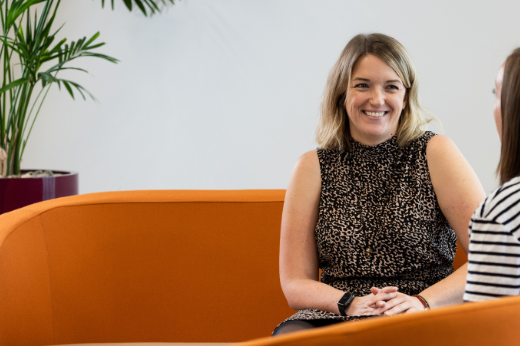 An image of Kim Masson sitting on an AAB couch and smiling at a colleague.