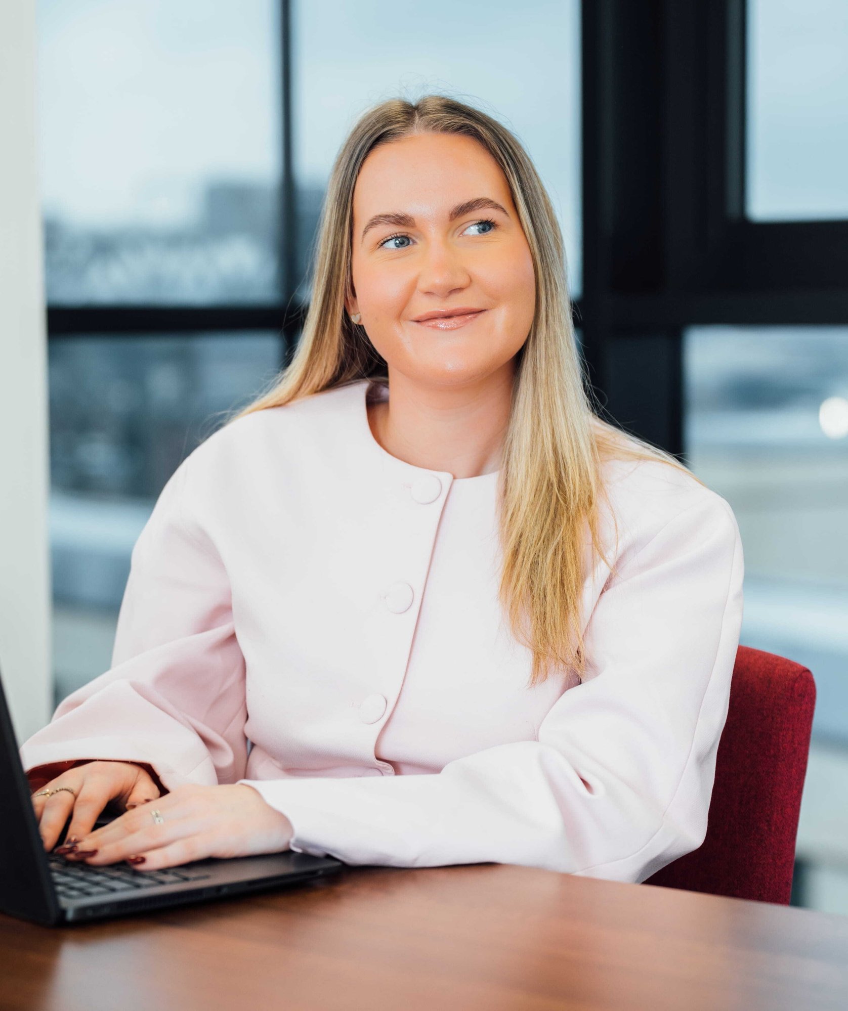 An image of Olivia Meldrum wearing a pink top and typing on a laptop.