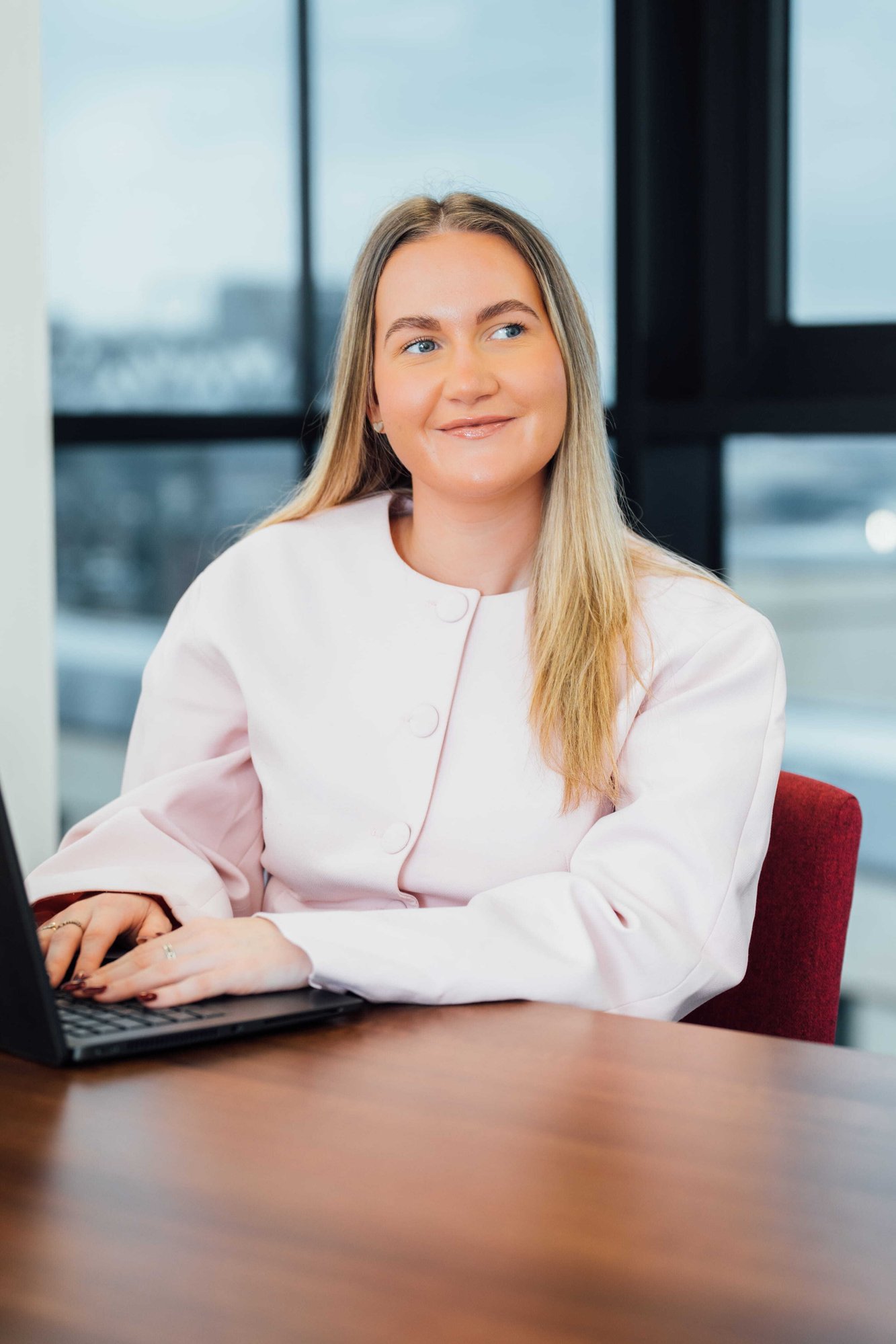 An image of Olivia Meldrum wearing a pink jacket and typing on her laptop.