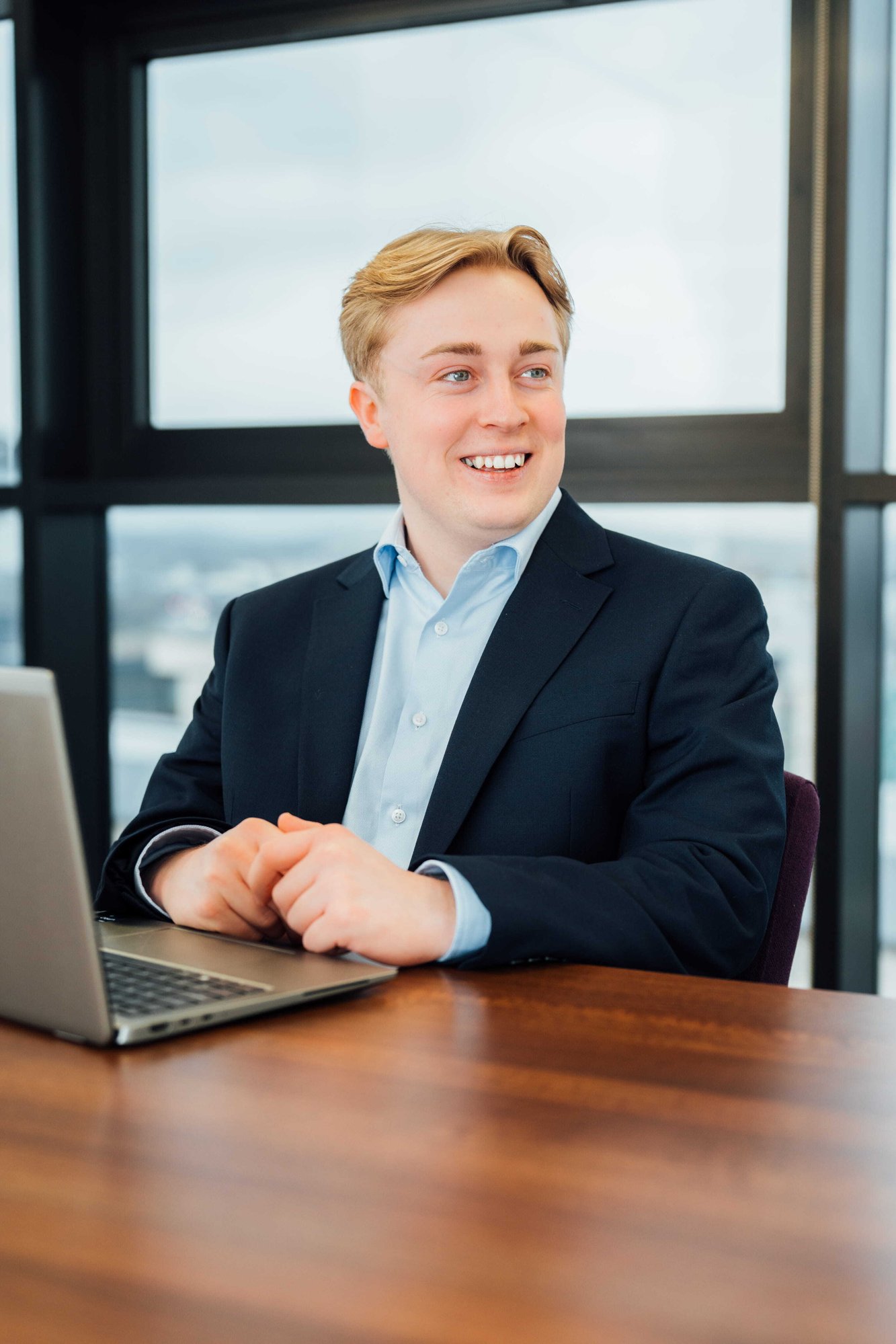An image of Robbie Boyle wearing a suit jacket and shirt. He is sitting on his laptop. 